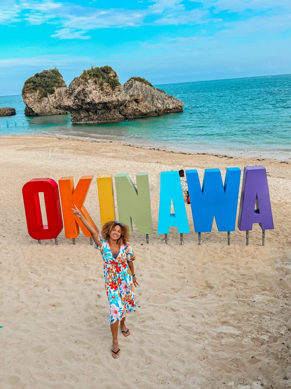 Gabby Beckford in front of the colorful Okinawa sign on a beach in Okinawa, Japan