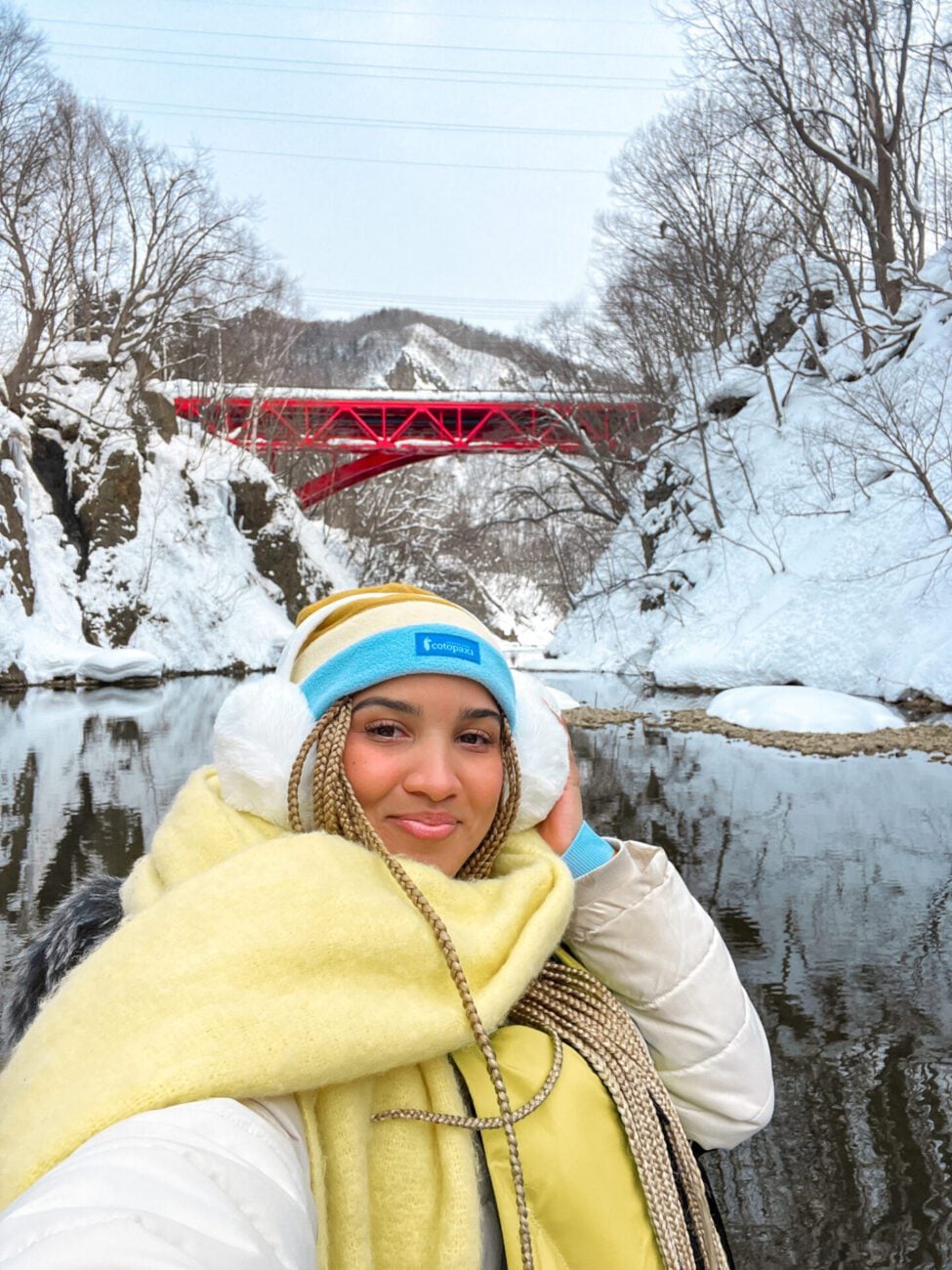Gabby Beckford smiling in front of a red bridge over a snowy river gorge in Hokkaido